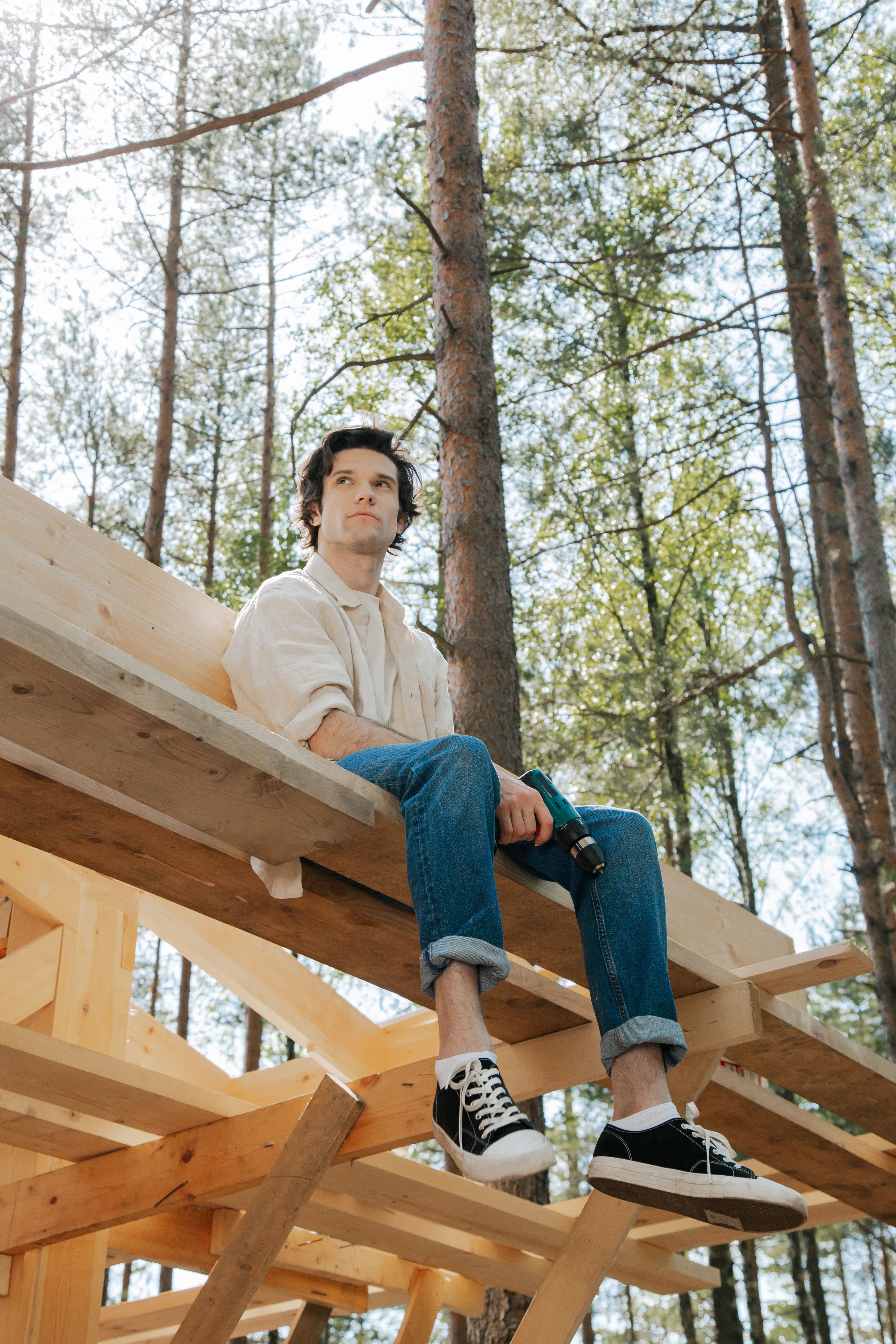 Young man sitting on a wooden structure outdoors, looking contemplative.