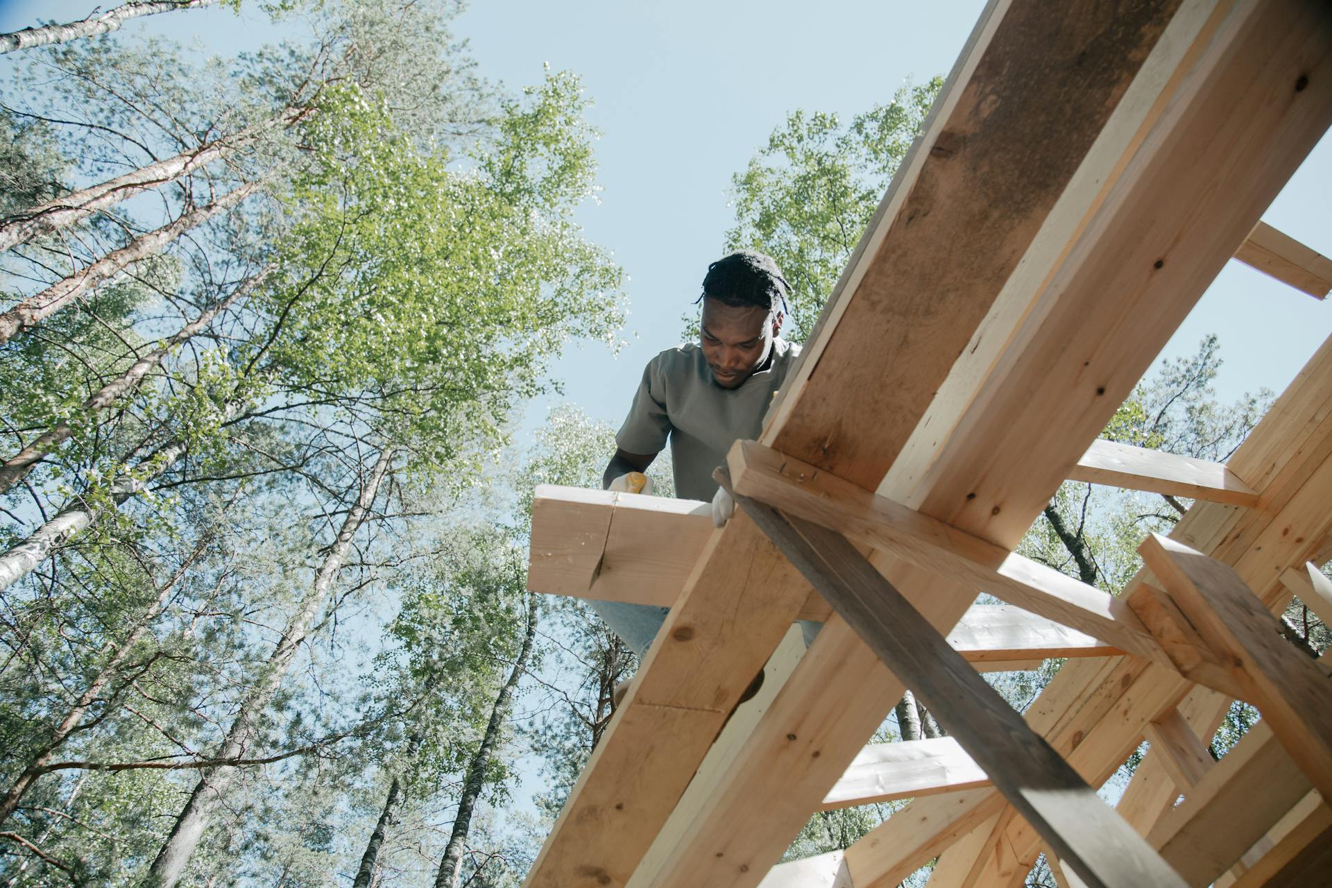 Black male carpenter working on a wooden frame outdoors, showcasing detailed craftsmanship.