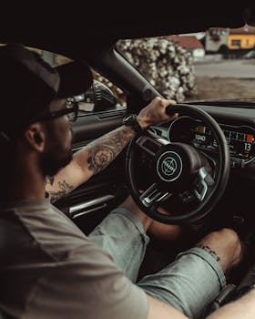 A tattooed man driving a luxury car in summer, showcasing modern car interior and technology.