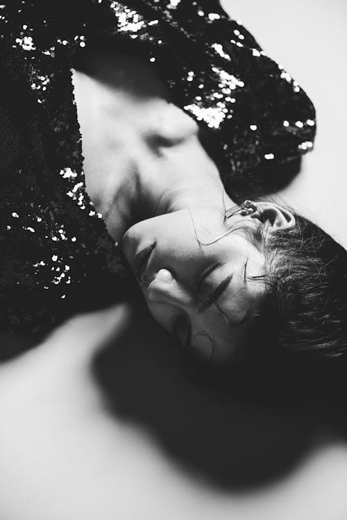 Grayscale Photo of a Woman Lying on White Surface