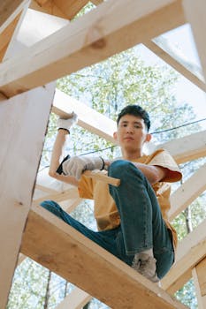 Young carpenter building wooden structure outdoors in sunlight, showcasing construction skills.