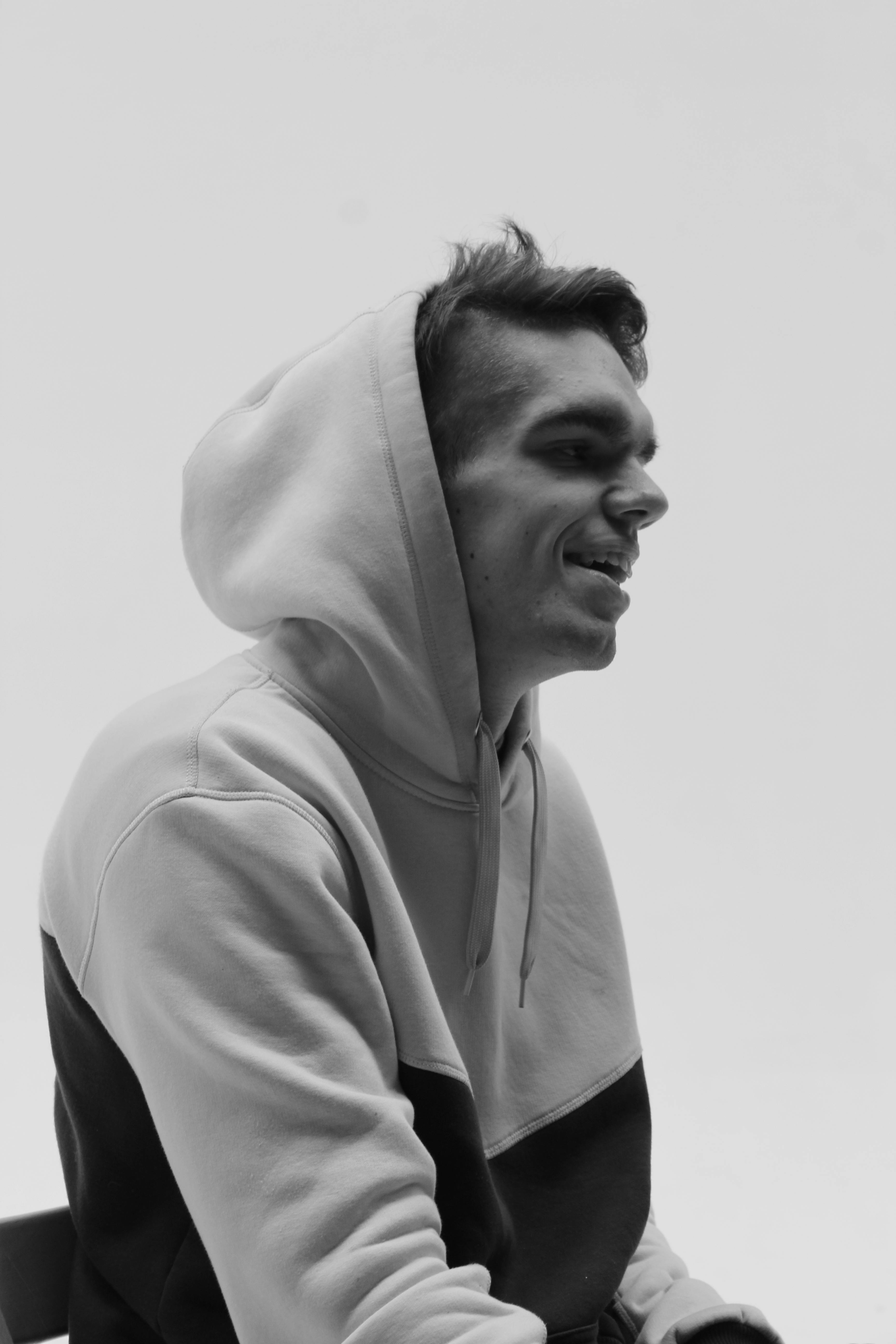 Profile view of a young man smiling in a hoodie, black and white photo.
