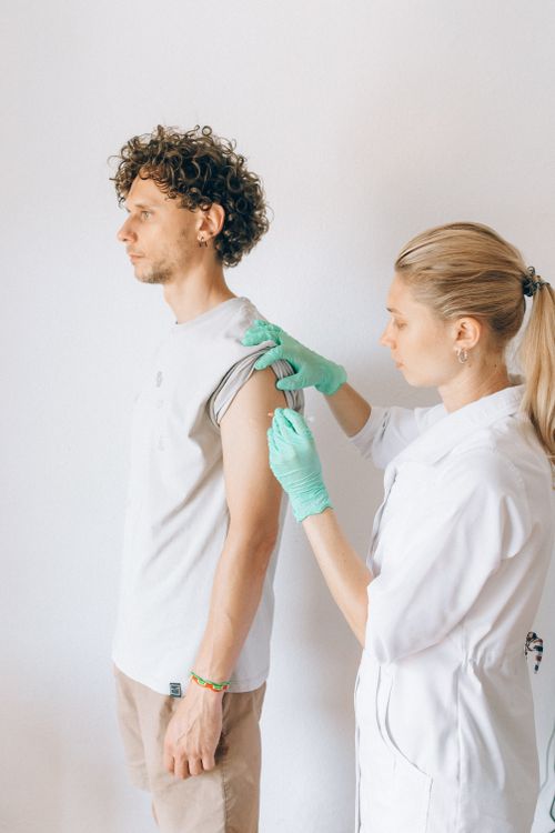 Free Nurse giving a vaccination to a man indoors, emphasizing healthcare and pandemic prevention. Stock Photo