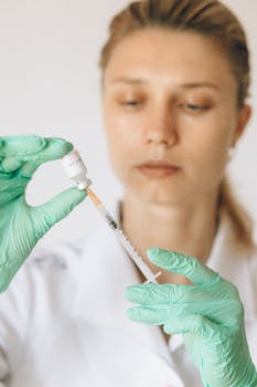 Woman healthcare worker with gloves preparing a vaccine syringe indoors.