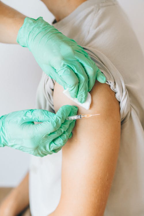 Person Wearing Latex Gloves Vaccinating a Man in Gray Shirt