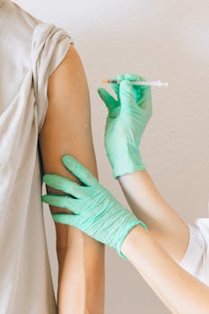 Close-up of gloved hands giving a vaccine injection to a patient's arm.