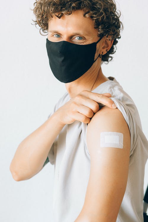 Man in White Shirt Wearing Black Face Mask Showing Vaccination on Arm