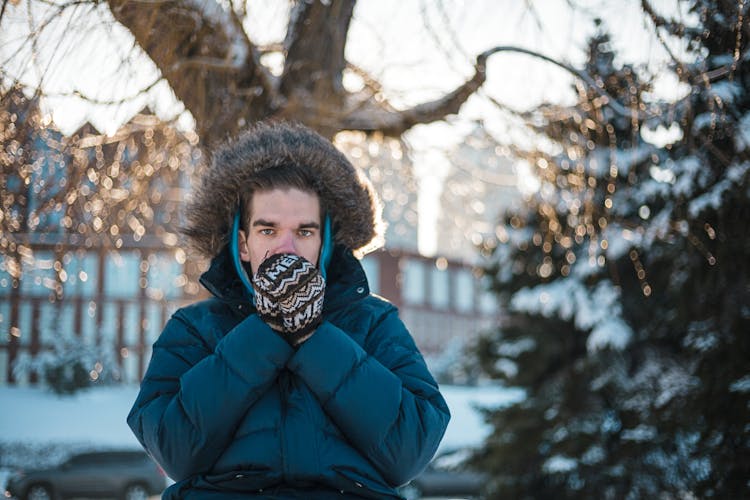 Man In A Winter Coat Blowing On Hands In Mittens 