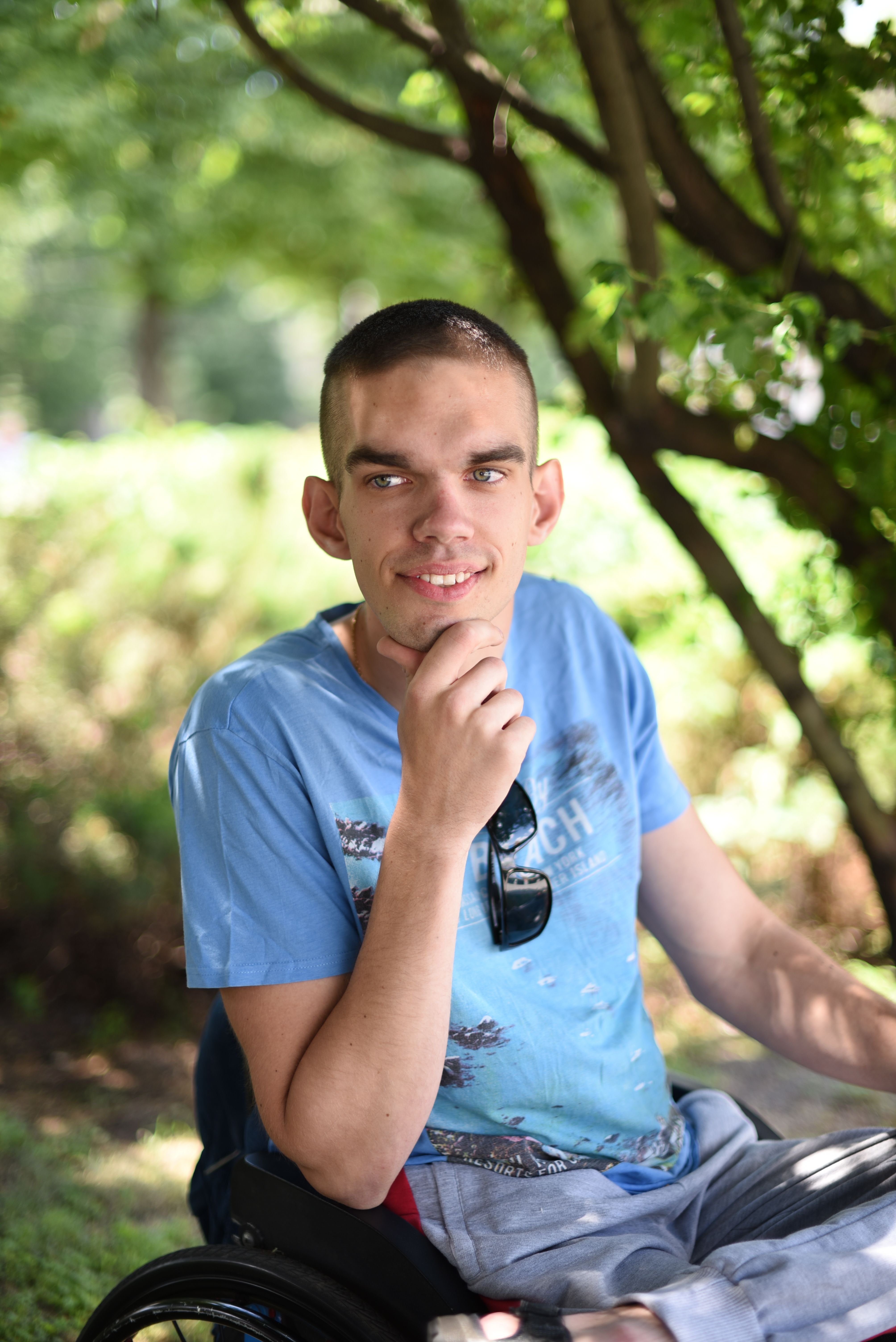 Casual outdoor portrait of a young man smiling in a park, sitting in a wheelchair.