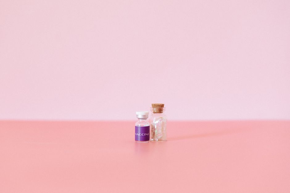 A small vaccine vial and glass container on a pink surface, showcasing minimalism.