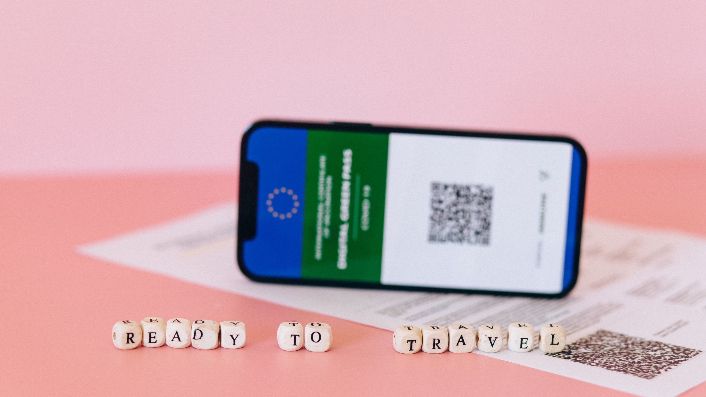 Smartphone displaying digital green pass on a pink surface with travel beads.