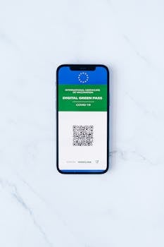 A smartphone displaying a digital green pass with QR code on marble surface.