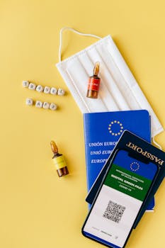 Flat lay of travel essentials including passport, mask, vaccine vials, and digital green pass.