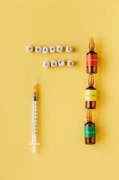 Flat lay of vaccine vials and syringe with travel safety message on yellow background.
