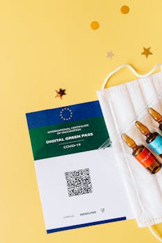 Close-up of a digital vaccination certificate with ampules and face mask on yellow background.