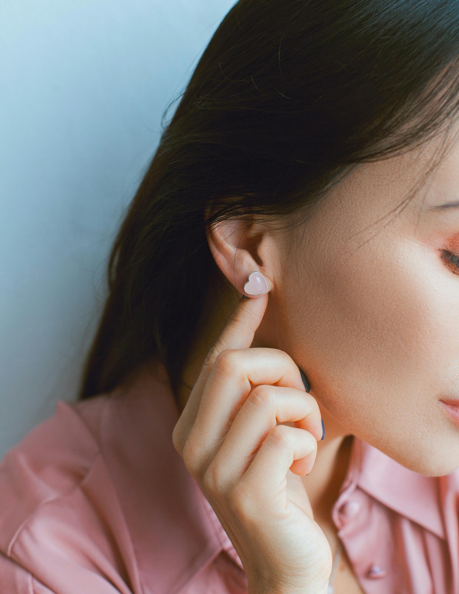 Close-up of a woman showcasing a heart-shaped earring in a serene pose.