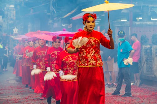 A Group of People  Wearing Red Costumes and Masks  Holding Umbrellas in a Parade 