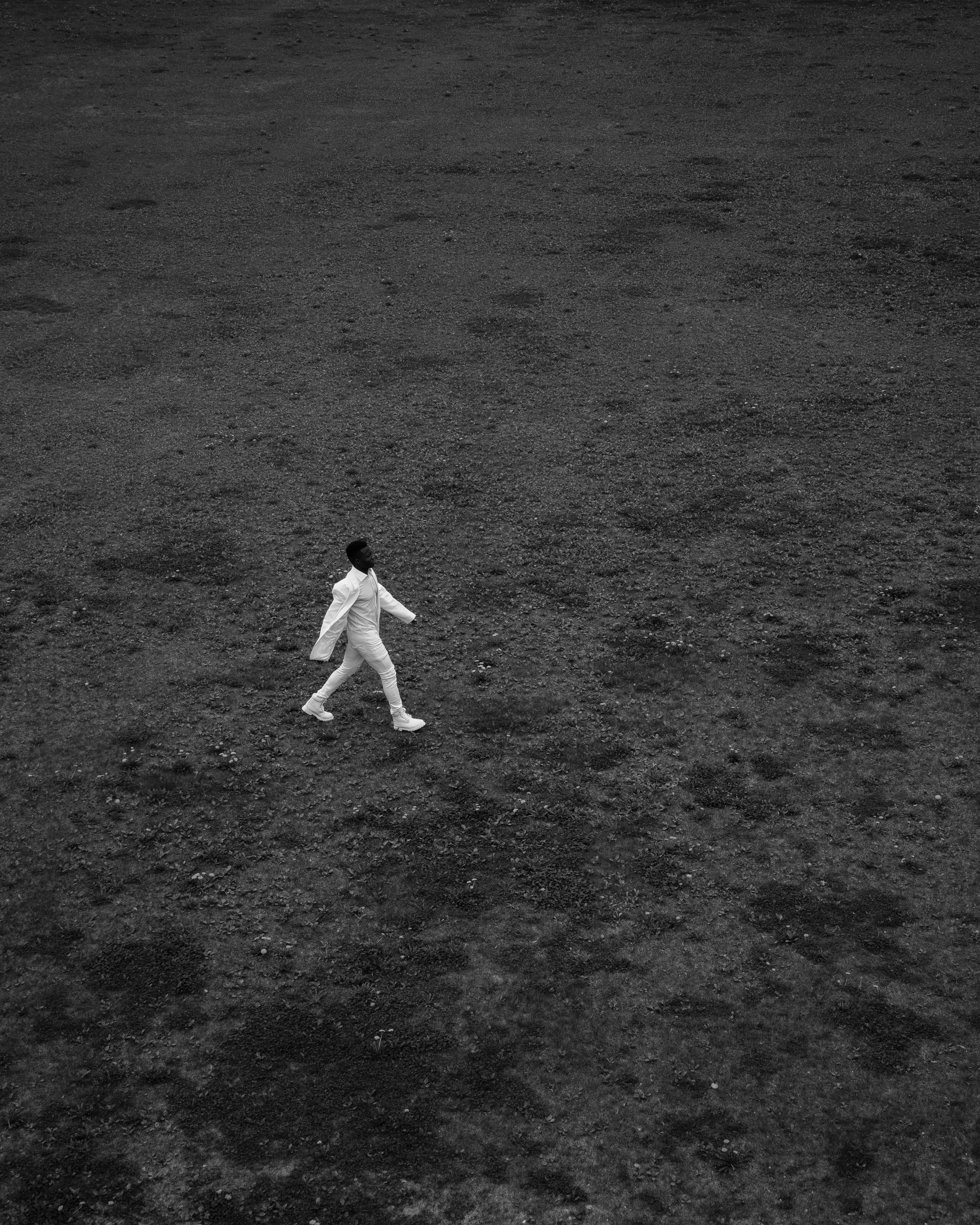 An individual in a white outfit walking across a vast, empty landscape captured in black and white.