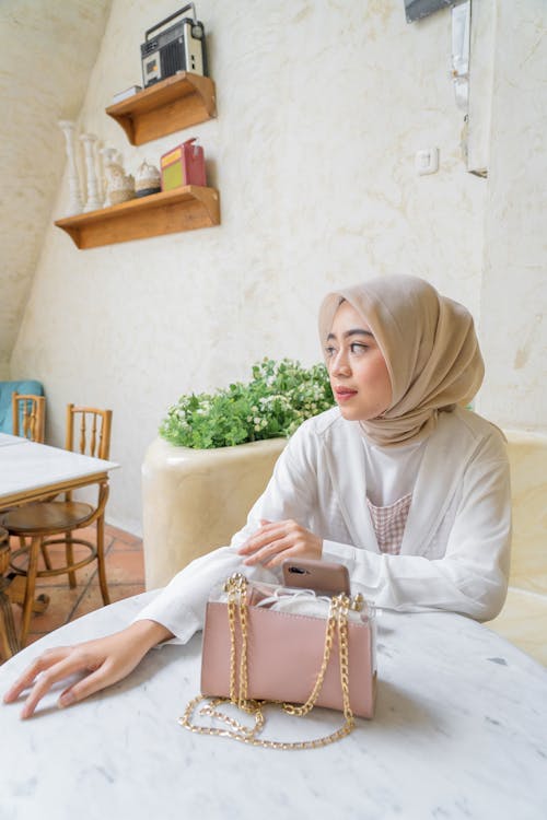 Free Woman in Tan Hijab and White Long Sleeves Sitting on Chair  Stock Photo