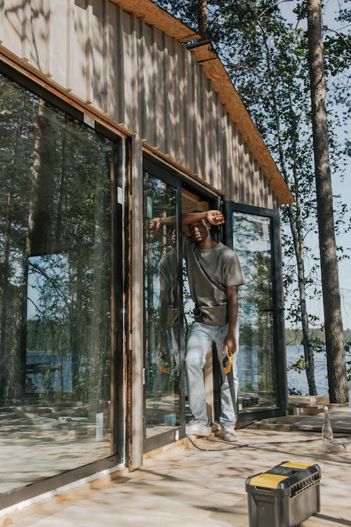 Free A Man in Gray Shirt and Denim Pants Standing Near the Wooden Cabin Stock Photo