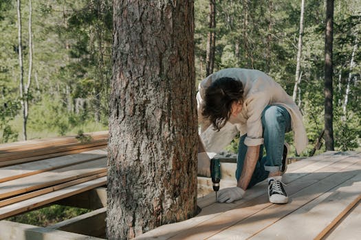 A man performs manual labor using a drill on a forest boardwalk construction project.