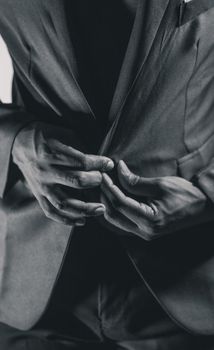 A monochrome image showing a person buttoning a suit jacket, capturing the elegance and detail of formal wear.