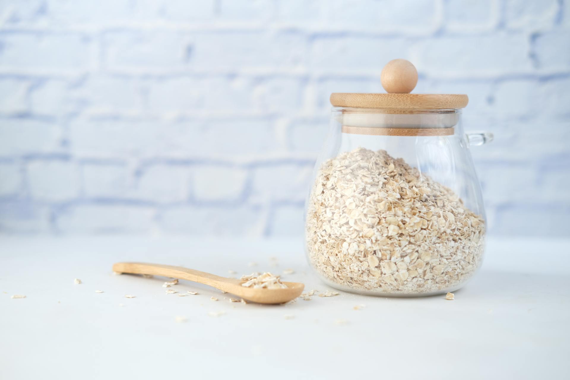 Close-up of organic oats in a glass jar with a wooden spoon on a light blue background.