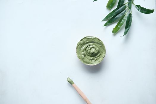 A calming green clay mask in a bowl with bamboo leaves on a white background.