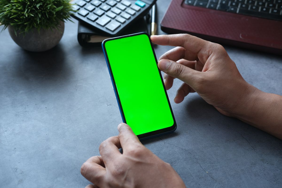Akıllı telefon tutan el, modern ofis masası arka planında