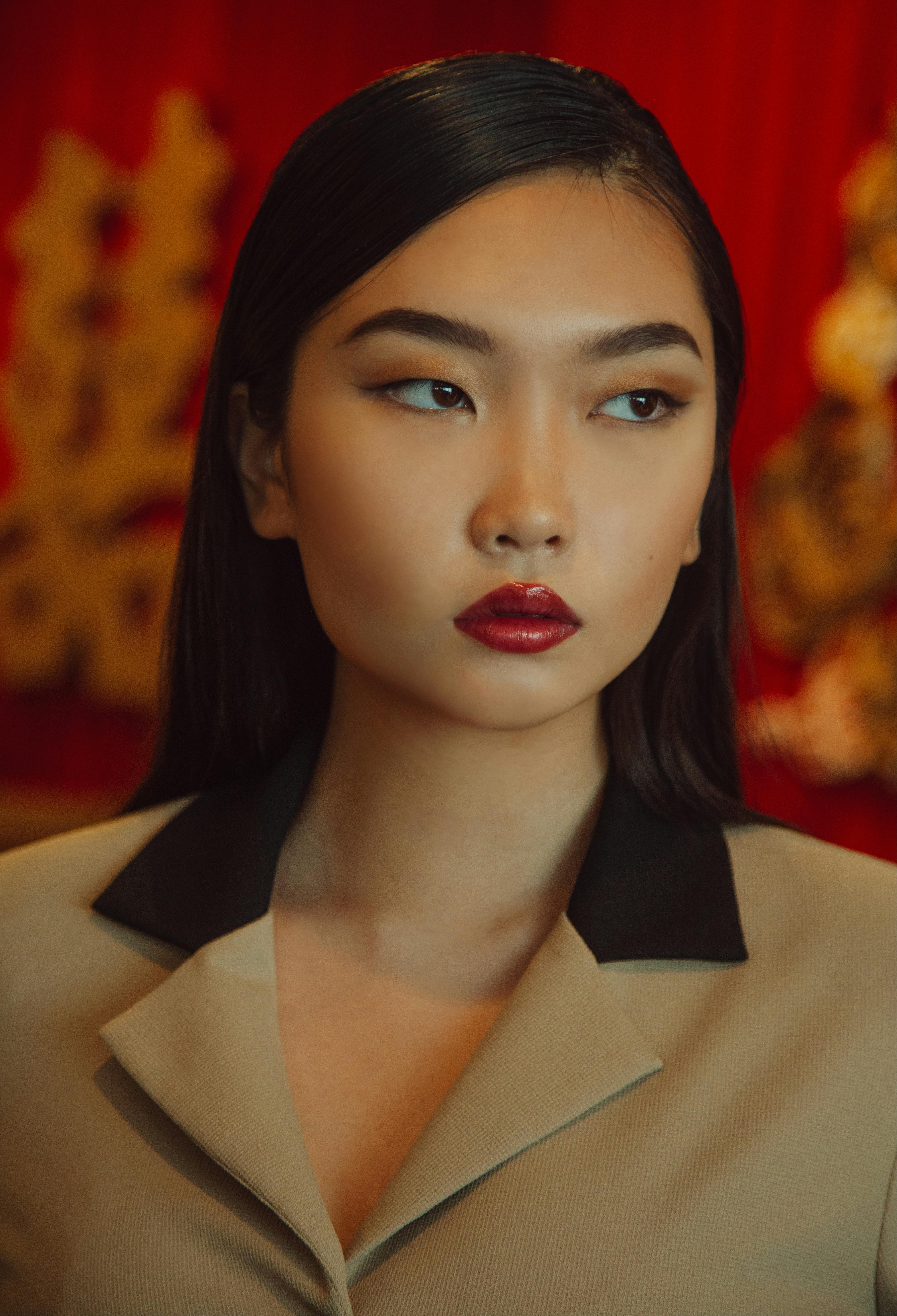 Close-up portrait of a stylish woman with red lips in front of a rich red backdrop.