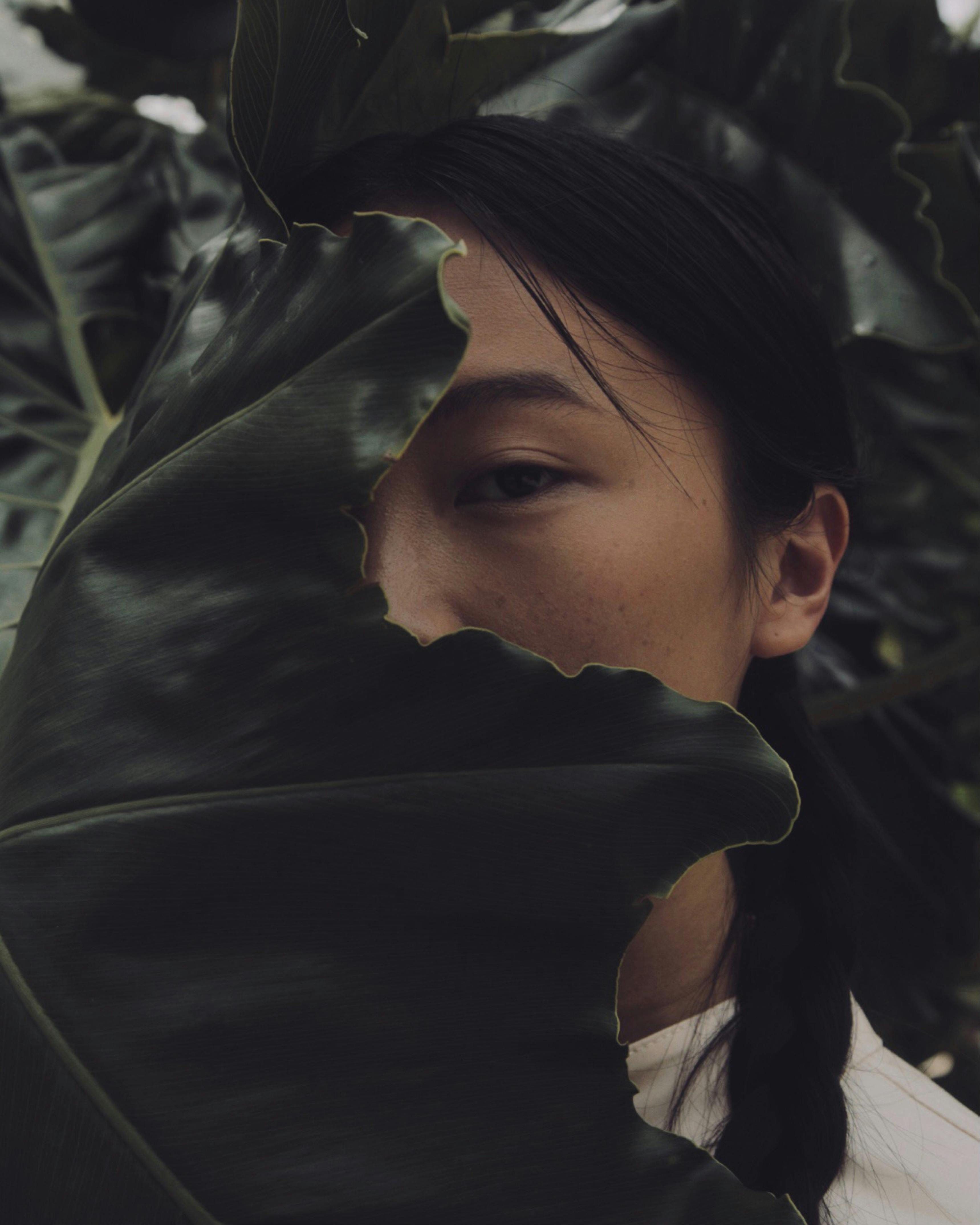 Close-up of a woman with a leaf covering half her face, outdoors.