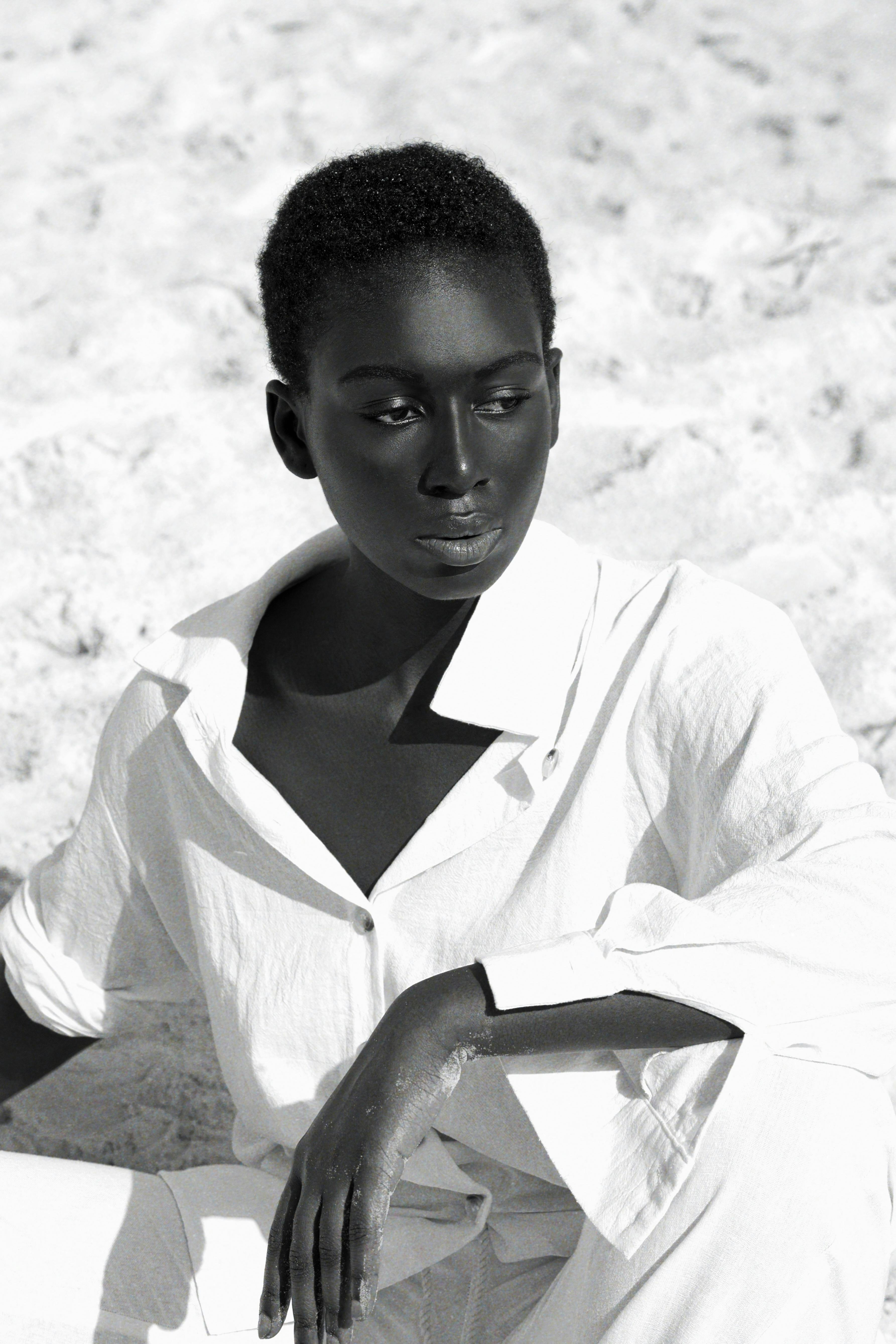 Black and white portrait of a woman in a white outfit on a beach, conveys elegance.