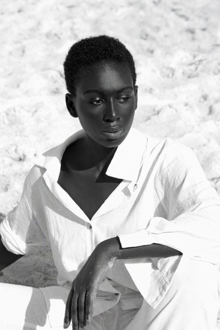 Black and white portrait of a woman in a white outfit on a beach, conveys elegance.