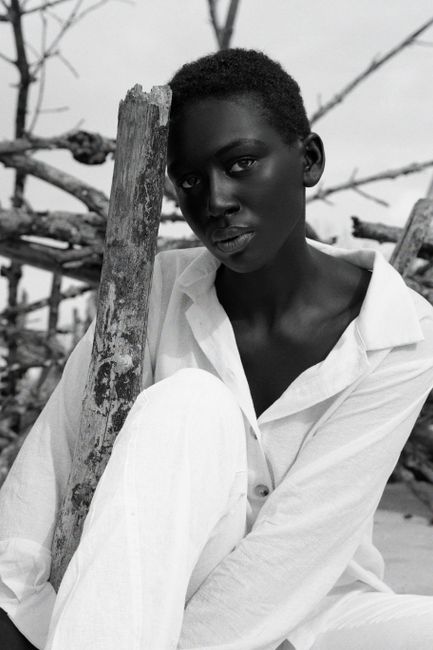 Monochromatic portrait of a woman in white attire posing outdoors with a wooden backdrop.
