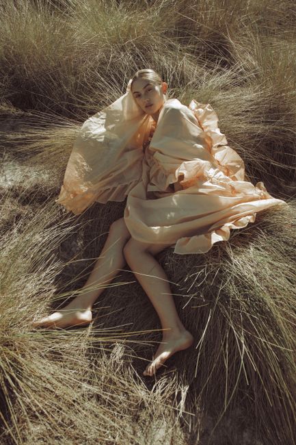 A woman poses elegantly in a flowing dress, surrounded by tall grass, capturing a serene outdoor moment.