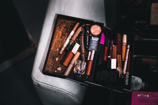 A cluttered cosmetic box filled with assorted makeup items and scattered glitter, capturing a chaotic beauty scene.