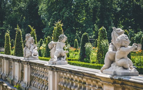 White Concrete Statues on Concrete Railing Beside the Garden