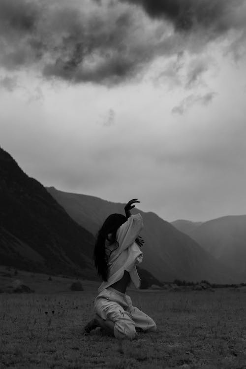 A Woman Kneeling on a Field Near the Mountains