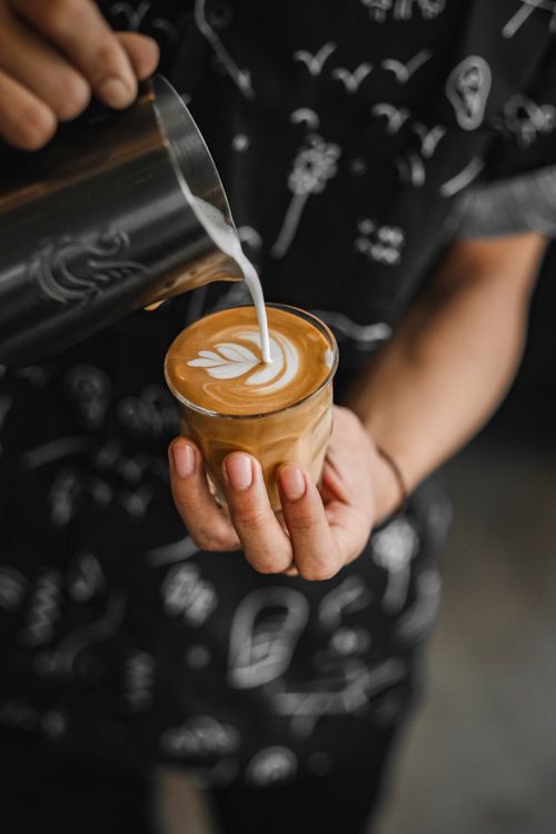 Free Detailed view of a barista's hand crafting latte art in a cafe, showcasing pouring technique. Stock Photo
