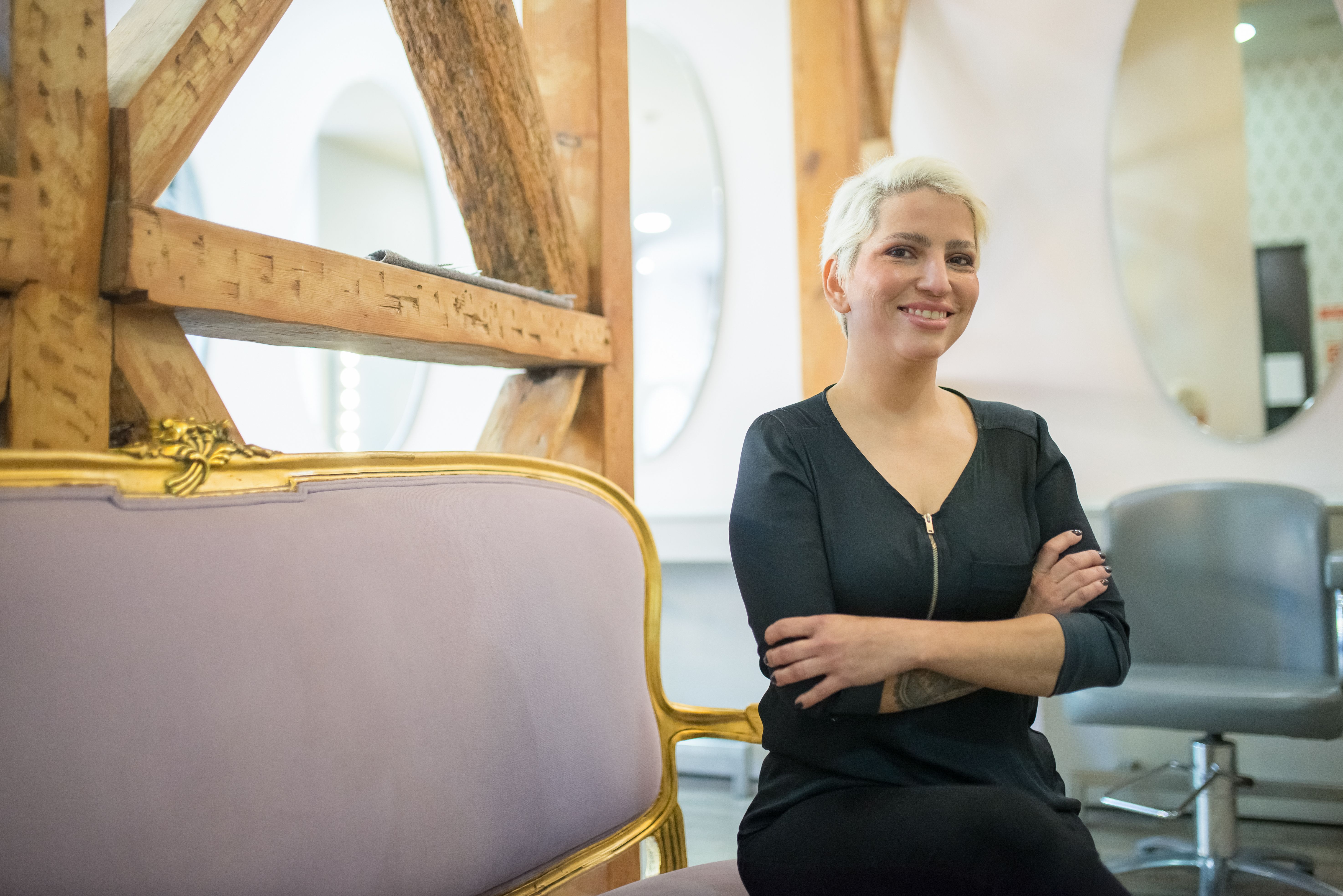 Woman with short hair and arms crossed smiling sitting on a stylish sofa indoors.
