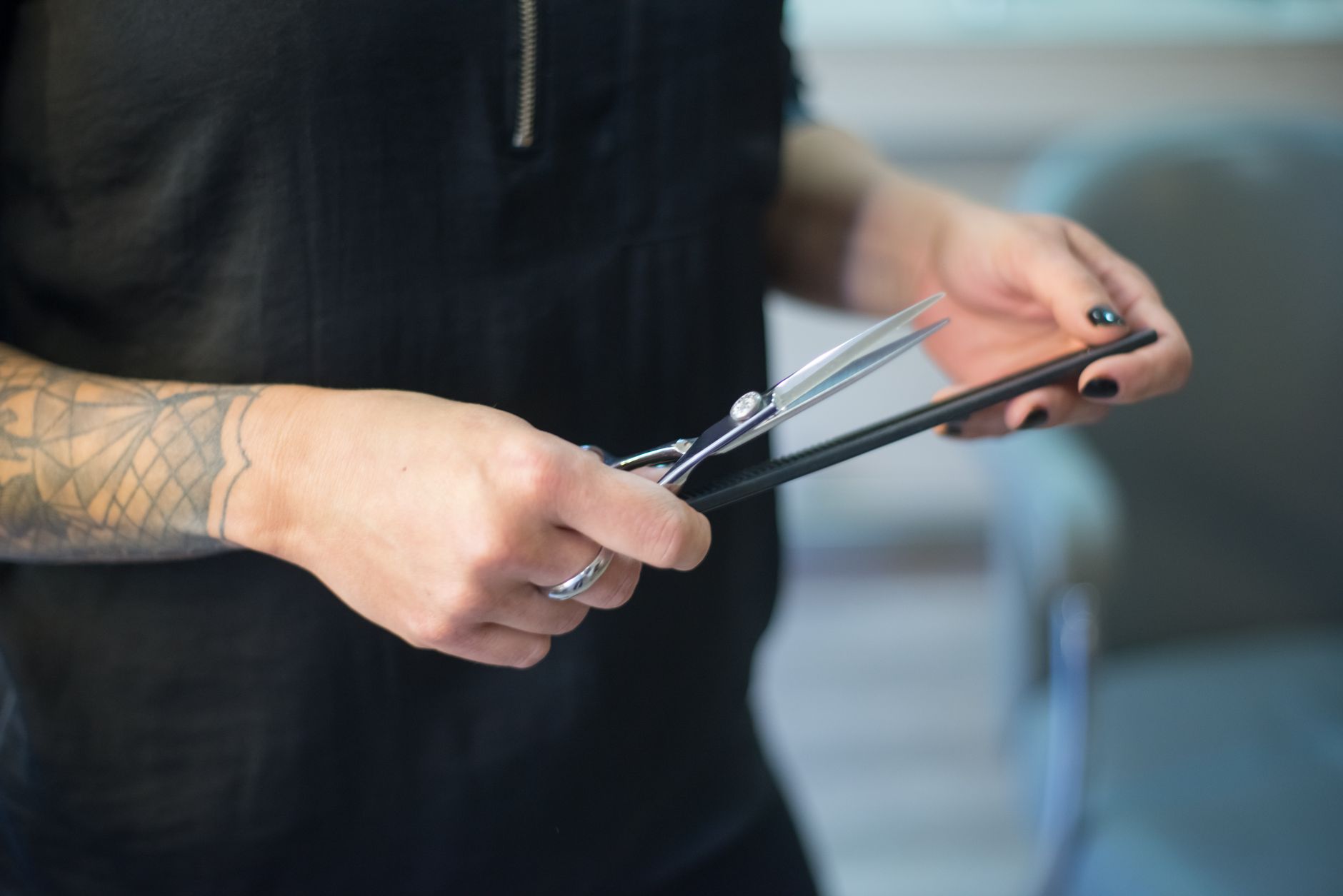 A hairdresser's hands holding scissors and a comb in a salon setting.