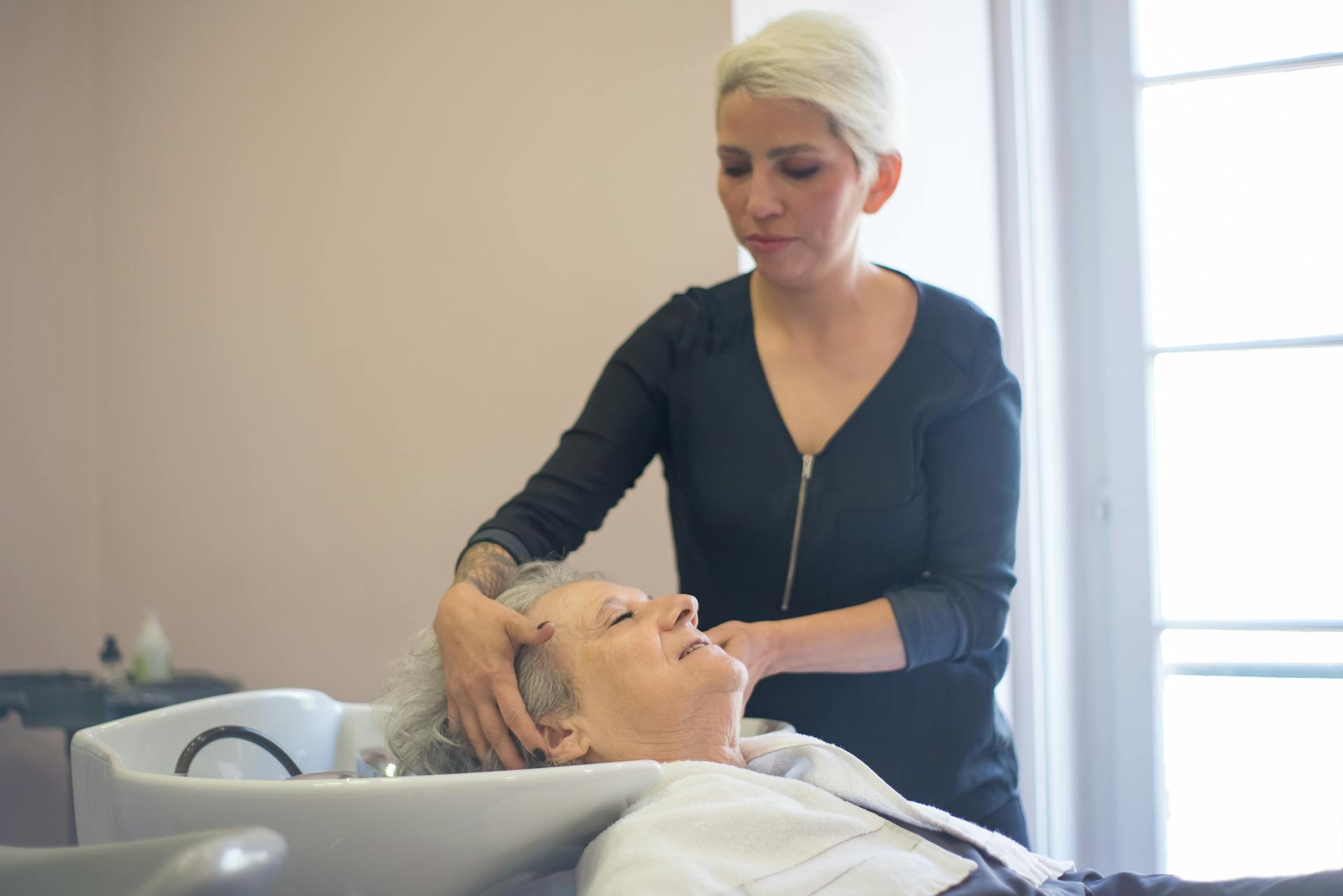 A hairdresser provides a relaxing washing service to an elderly woman in a salon.