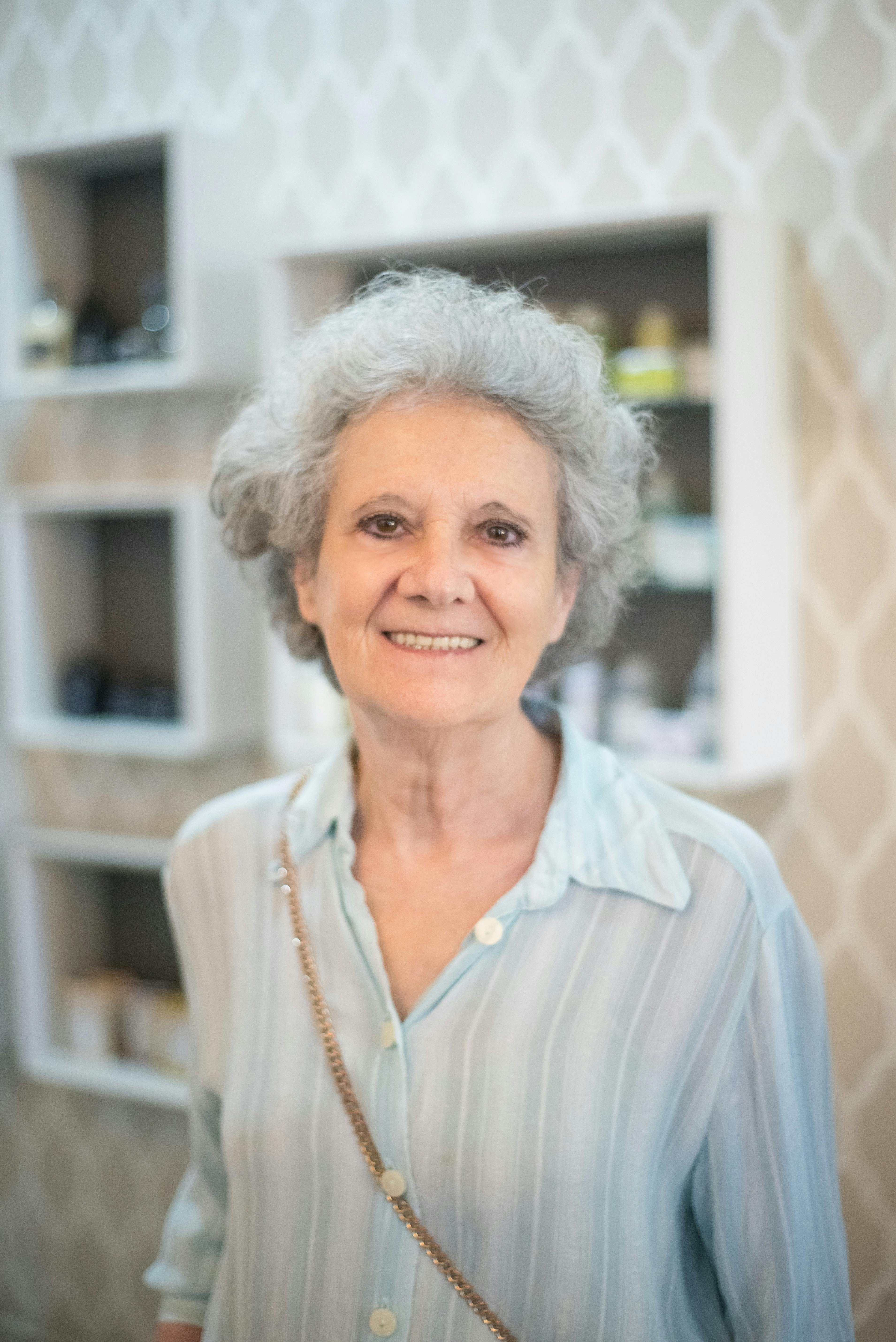 一位灰头发的老妇人站在室内的图案墙上，热情地微笑着