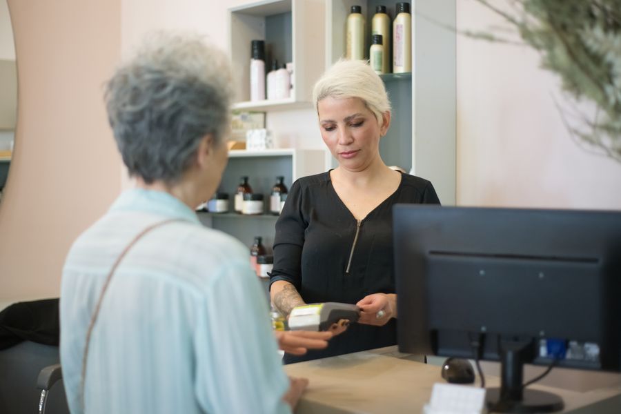 Two women at a hair salon checkout, one making a payment using a card reader.