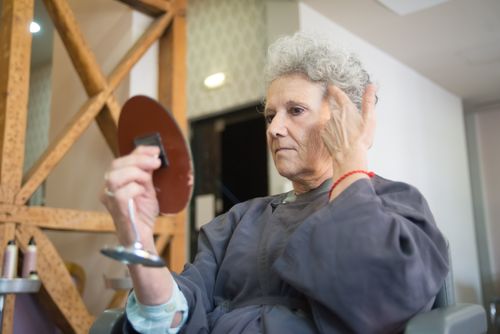 Free Elderly woman examining her new hairstyle in a salon while holding a handheld mirror. Stock Photo