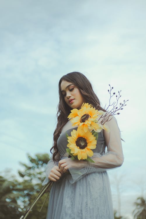 A Woman Holding Stems of Sunflowers while Looking Down