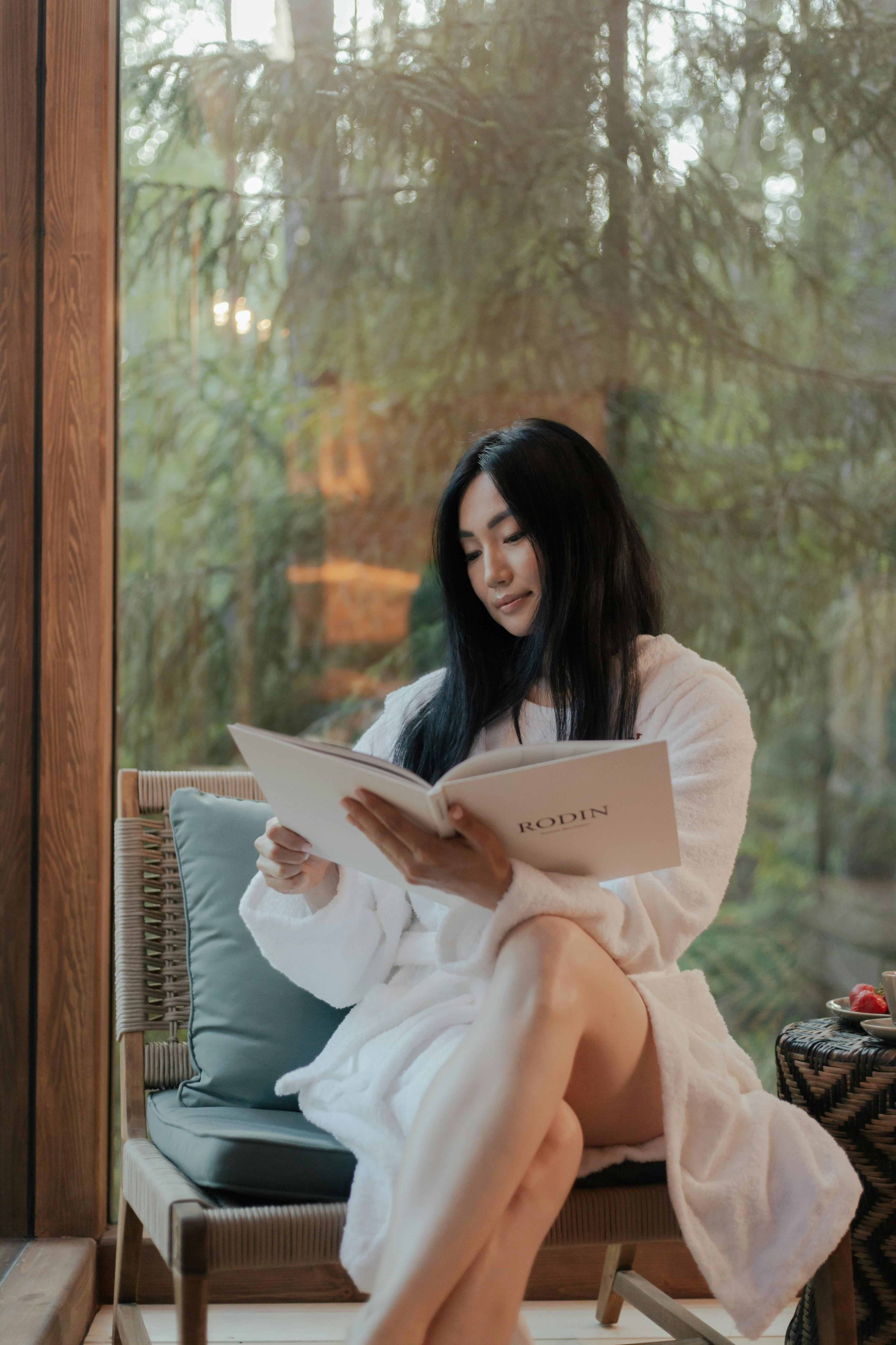 Asian woman enjoying a book in a cozy indoor setting, surrounded by nature.