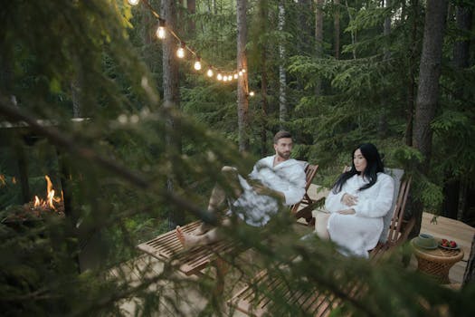 Couple in bathrobes enjoying a peaceful evening on a wooden deck in a forest.