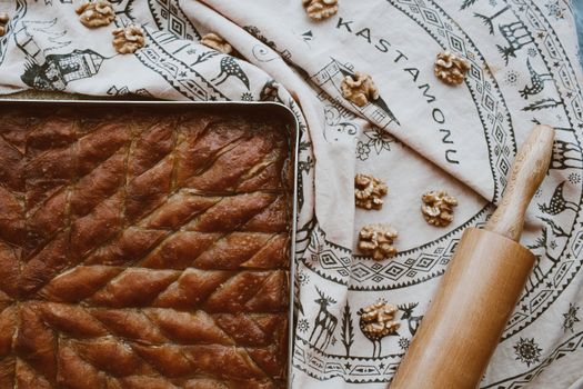 Delicious homemade baklava on a patterned cloth with walnuts and rolling pin.