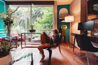 一位女士懒洋洋地躺在一间时尚的酒店房间里，透过大窗户欣赏着郁郁葱葱的绿地